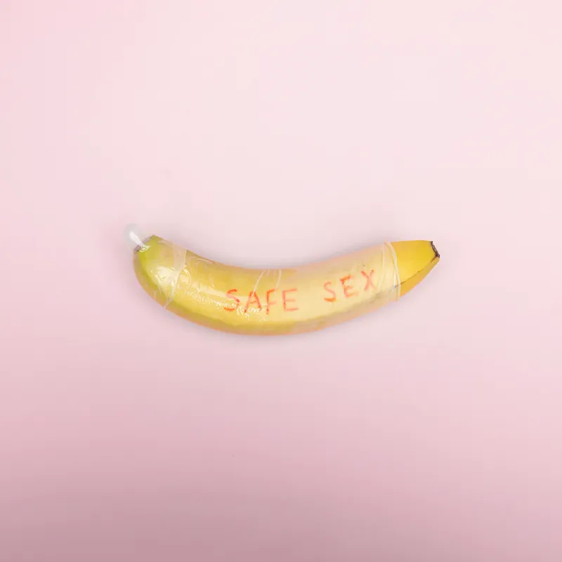 Un plátano con un preservativo puesto y la frase safe sex escrita encima