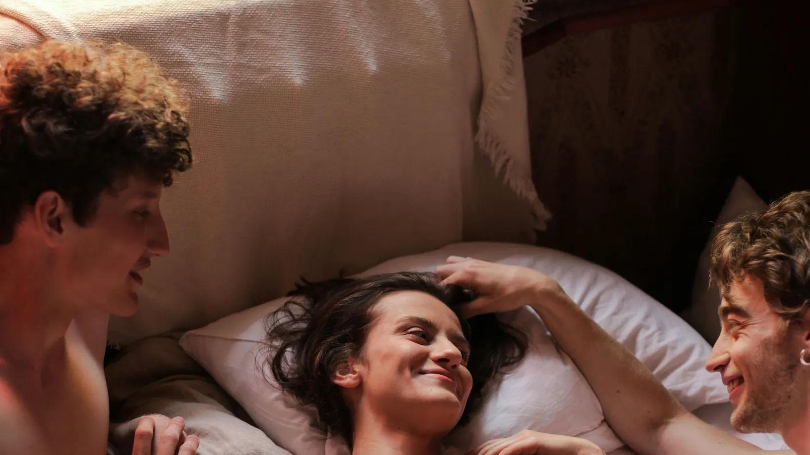 Tres personas en una cama, conversando con luz de tarde